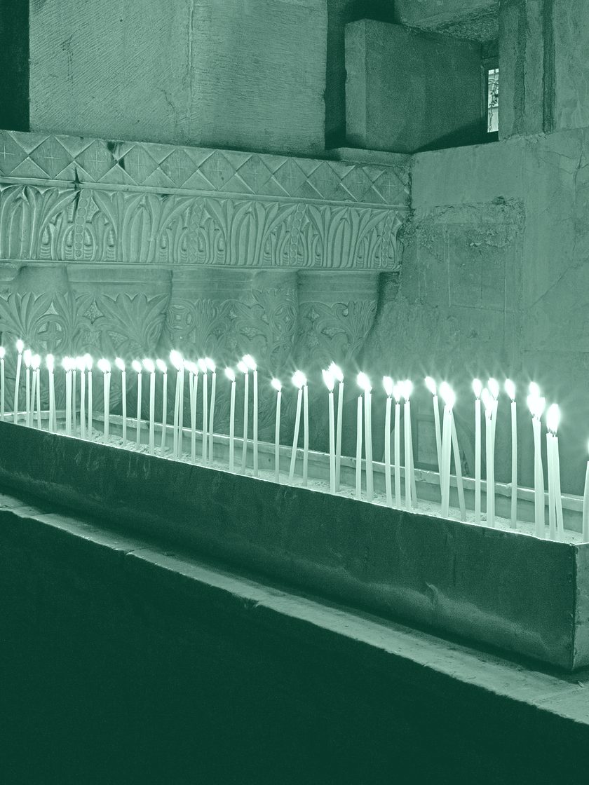 A long row of lit taper candles in a dark church, in deep green duotone