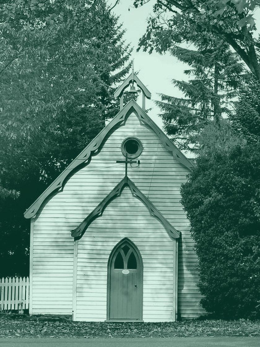 A small white timber church under trees, in deep green duotone