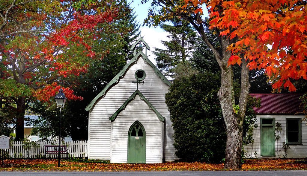 A small white timber church with green trim under autumn trees